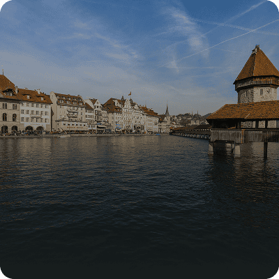 Ein Blick vom Flussufer auf historische Gebäude und die Kapellbrücke in Luzern, Schweiz, unter einem teilweise bewölkten Himmel.