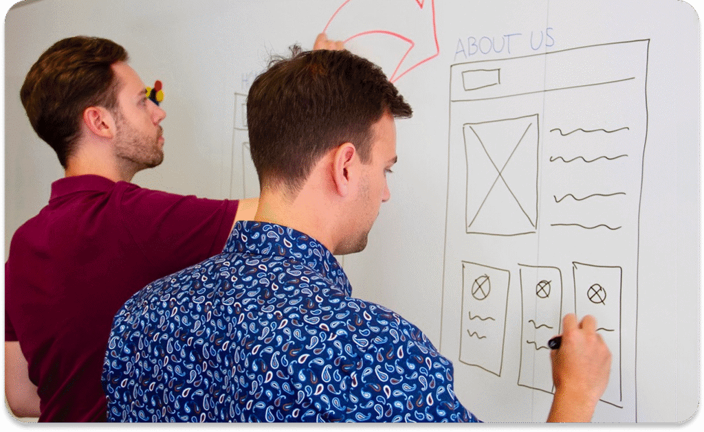 Zwei Männer zeichnen Website-Drahtgittermodelle und Diagramme auf ein Whiteboard und arbeiten gemeinsam an einem Design- oder Planungsprojekt.