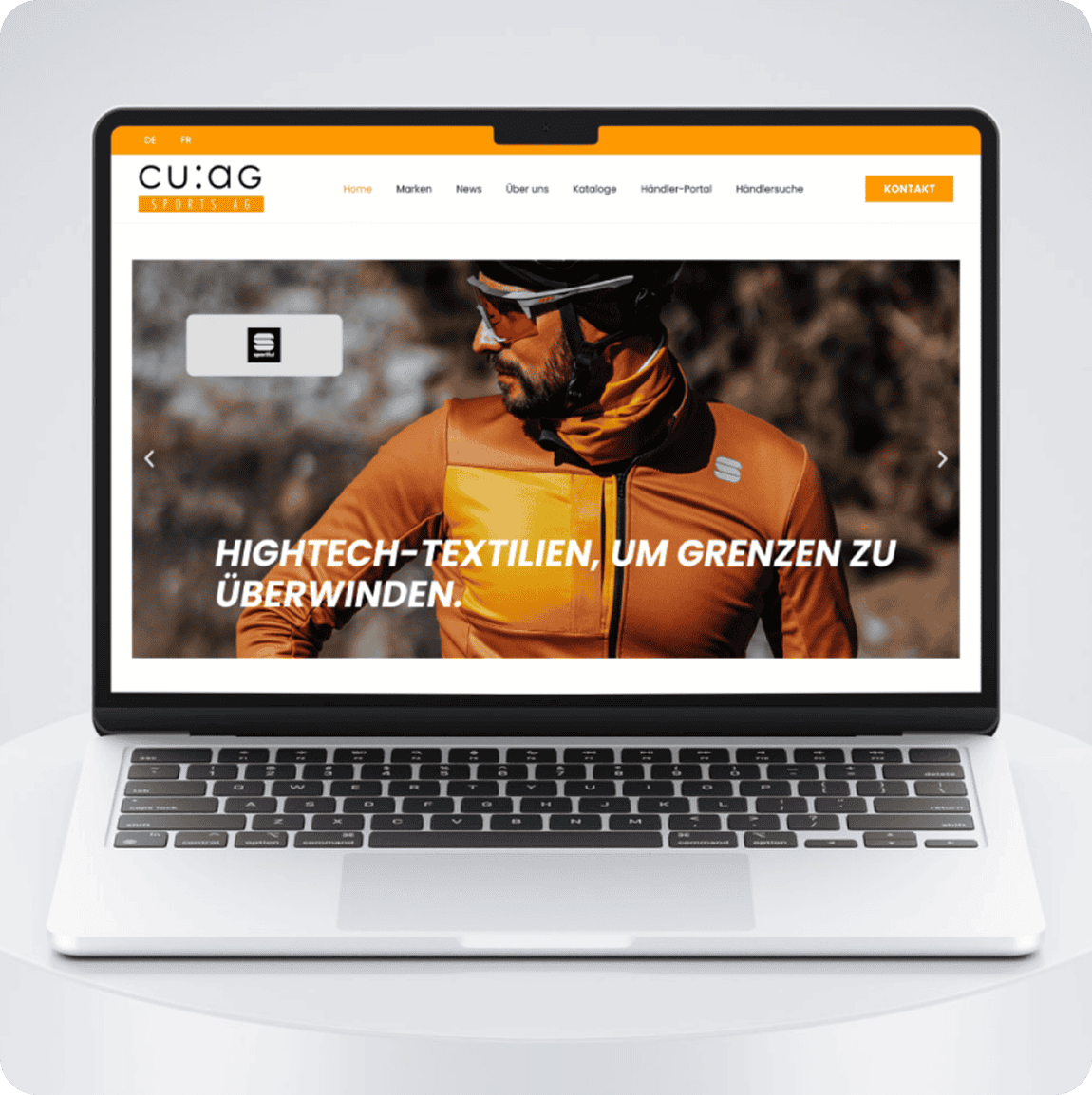 Ein Laptop zeigt die Website der CUAG Sports AG mit einem Mann in einer orangefarbenen Jacke und dem deutschen Text "HIGHTECH-TEXTILIEN, UM GRENZEN ZU ÜBERWINDEN.".