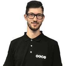 Ein Mann mit kurzen dunklen Haaren und Brille trägt ein schwarzes Poloshirt mit weißem „ALBI“-Schriftzug auf der Brust und steht vor einem dunklen Hintergrund.