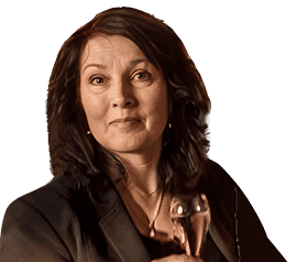 Frau mit schulterlangem dunklem Haar, trägt einen dunklen Blazer, hält eine Glasauszeichnung und blickt mit neutralem Gesichtsausdruck in die Kamera.