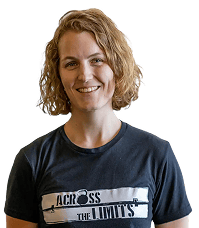 Eine Person mit kurzen lockigen Haaren und einem marineblauen T-Shirt mit der Aufschrift „ACROSS THE LIMITS“ steht lächelnd vor der Kamera.