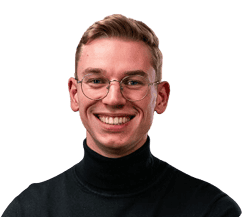 Ein junger Mann mit kurzen hellbraunen Haaren, einer runden Brille und einem schwarzen Rollkragenpullover lächelt vor einem schlichten Hintergrund in die Kamera.