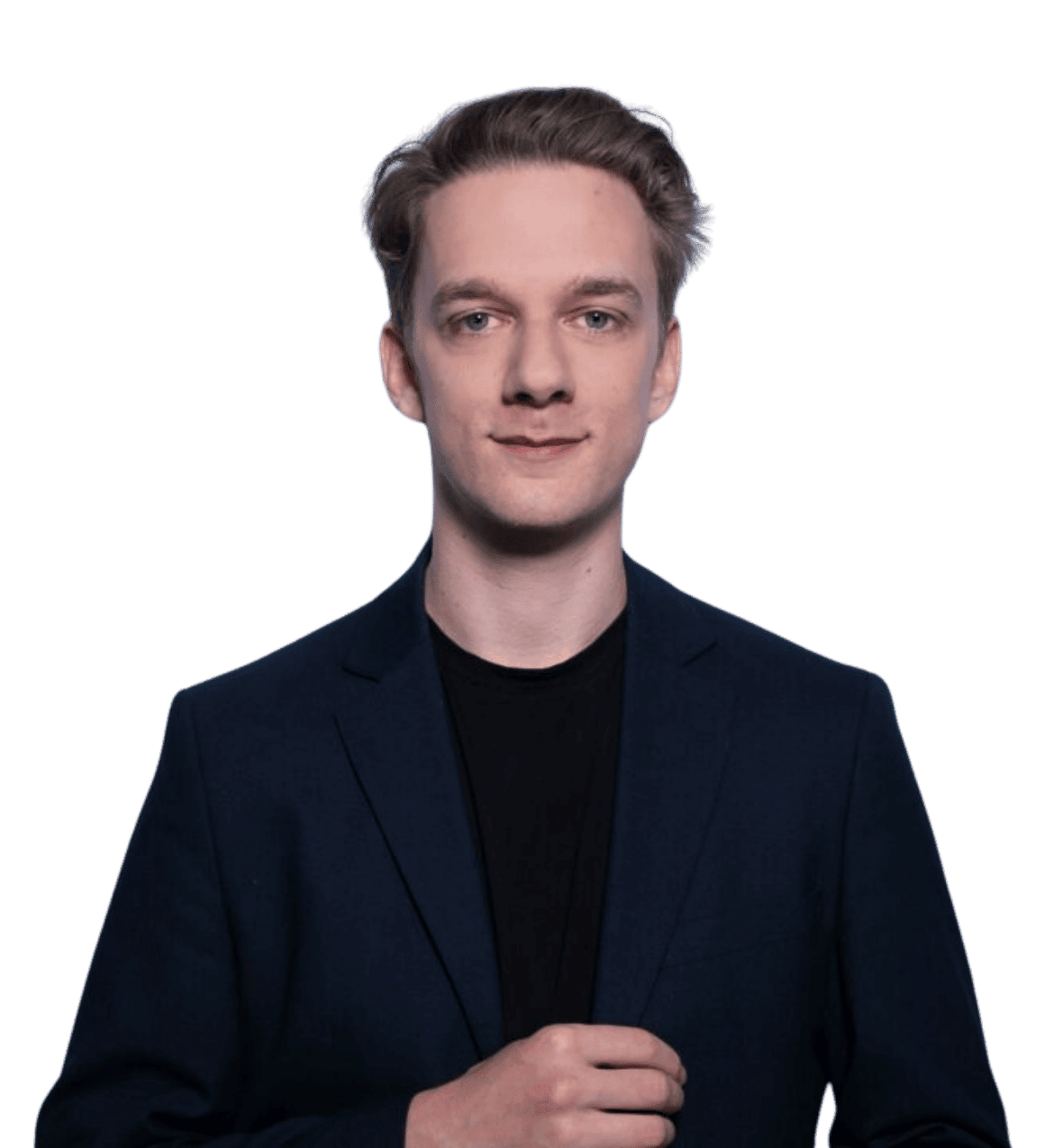 Ein junger Mann mit kurzen, hellbraunen Haaren, einem dunklen Blazer und einem schwarzen Hemd steht vor einem schlichten, grünen Hintergrund.