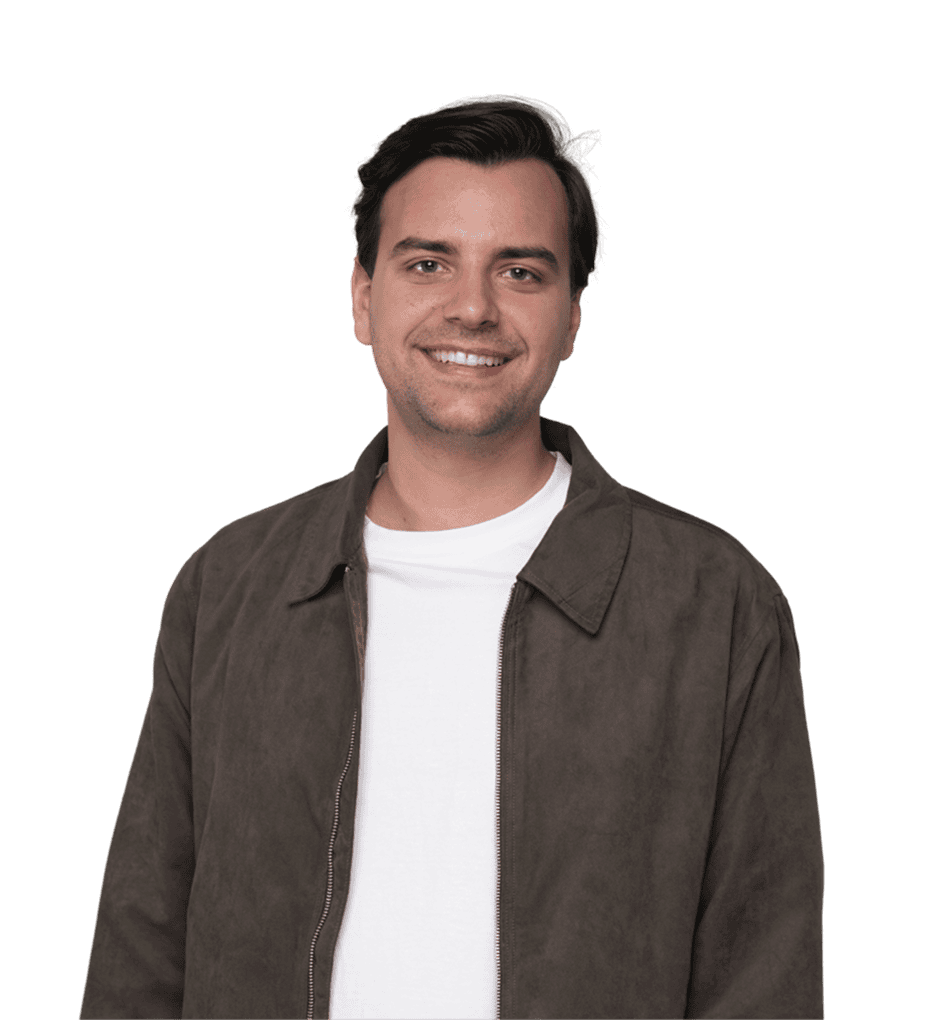 Ein Mann mit kurzen dunklen Haaren, der eine braune Jacke über einem weißen T-Shirt trägt, steht und lächelt vor einem schlichten Hintergrund.